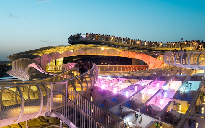 Visitors walking on Setas de Sevilla's illuminated walkways at sunset, Spain.