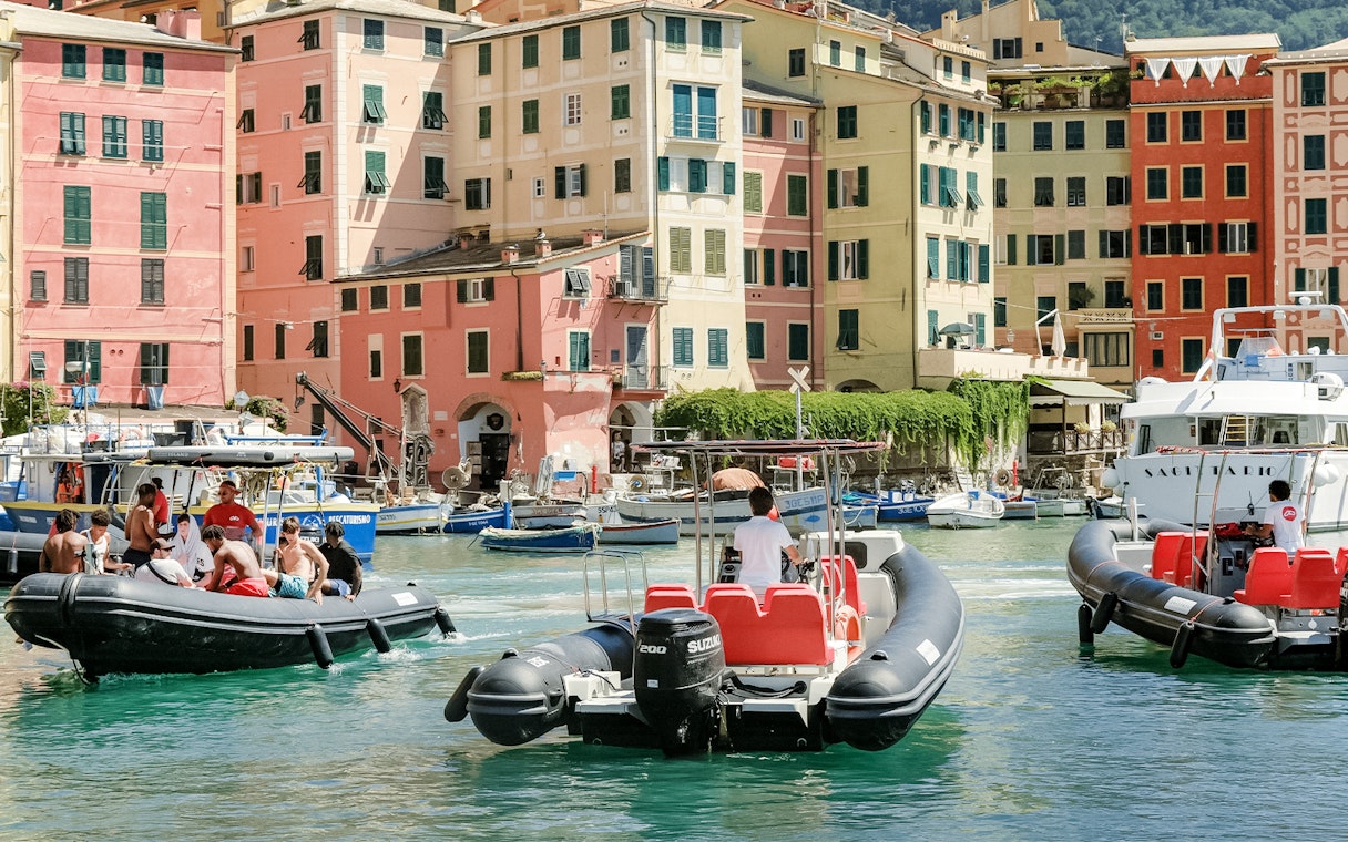 Boats with tourists in Cinque Terre harbor, colorful buildings in background, La Spezia tour.
