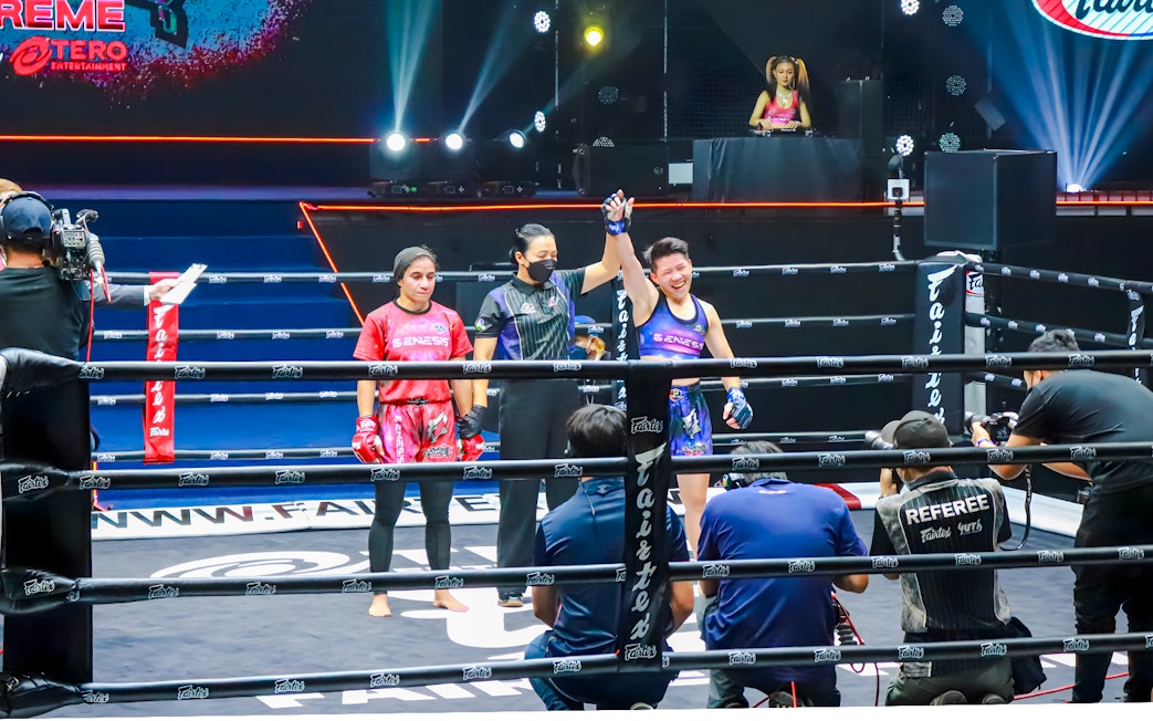 Muay Thai fighters at One Lumpinee Boxing Stadium, referee raising winner's hand.