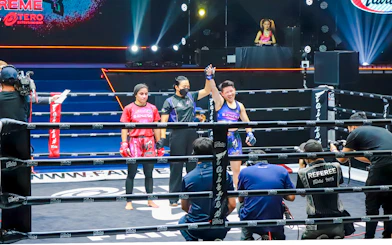 Muay Thai fighters at One Lumpinee Boxing Stadium, referee raising winner's hand.