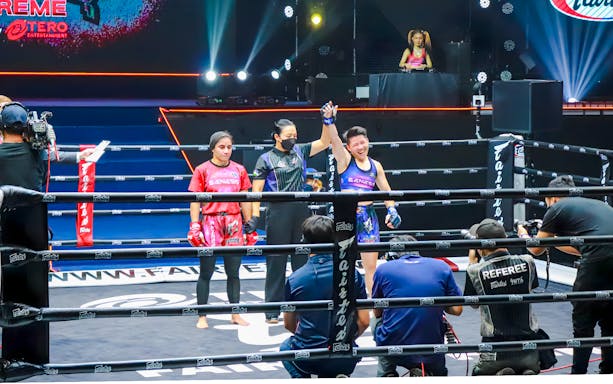 Muay Thai fighters at One Lumpinee Boxing Stadium, referee raising winner's hand.