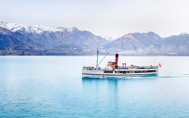 Steamboat cruising on Lake Wakatipu with snow-capped mountains in the background.