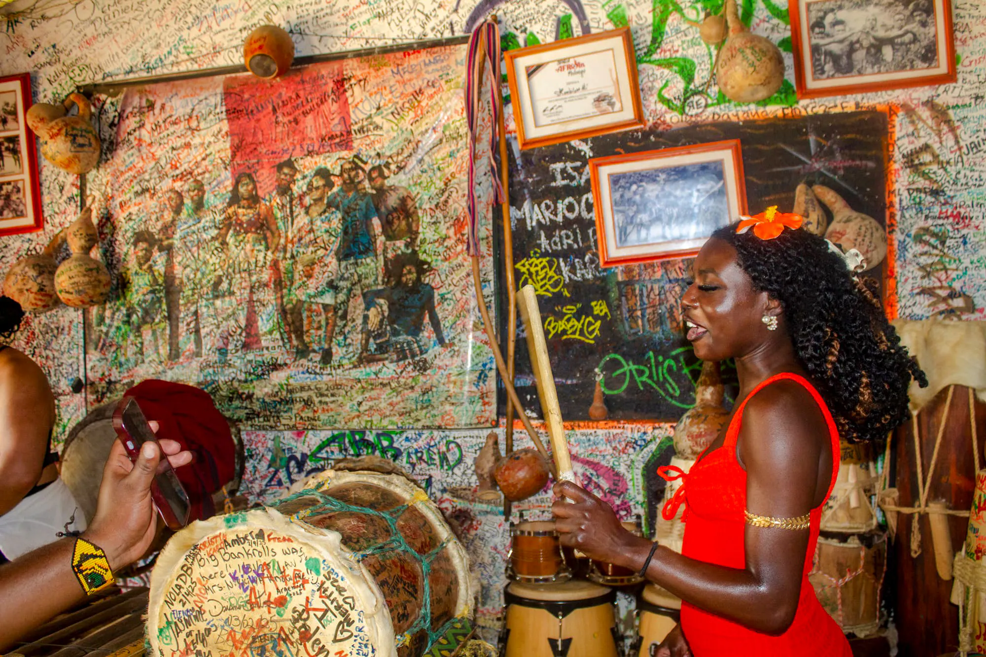Woman playing traditional drums in a colorful, graffiti-covered room in San Basilio de Palenque.
