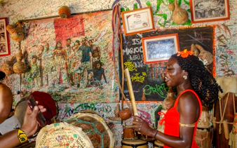 Woman playing traditional drums in a colorful, graffiti-covered room in San Basilio de Palenque.
