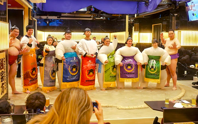 Visitors posing with sumo wrestlers at Asakusa Sumo Club, Tokyo.