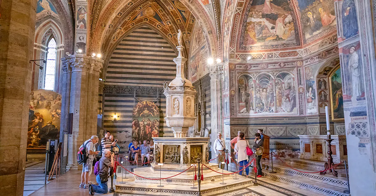 Tourists inside Siena Cathedral admiring frescoes and ornate architecture, Italy.