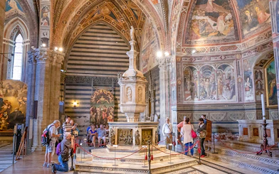 Tourists inside Siena Cathedral admiring frescoes and ornate architecture, Italy.