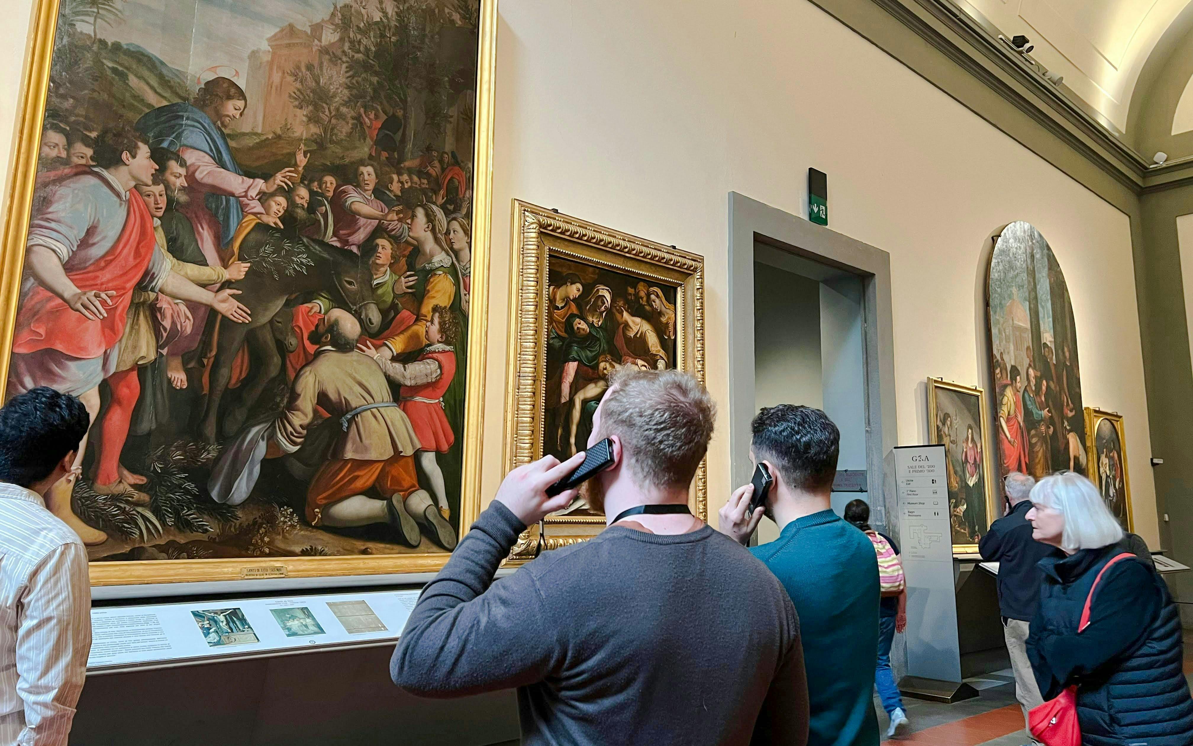 Visitors using audio guides at Academia Gallery, Florence, viewing Renaissance paintings.