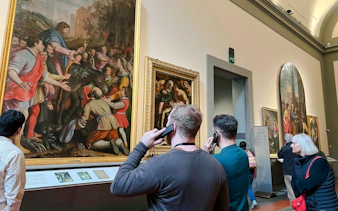 Visitors using audio guides at Academia Gallery, Florence, viewing Renaissance paintings.