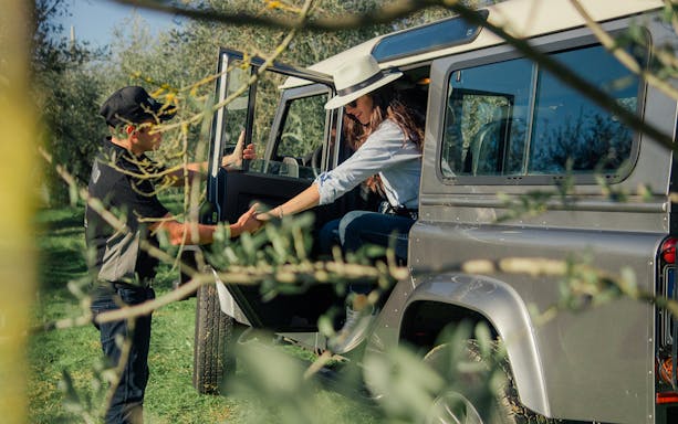 Tour guide assisting a guest from a safari vehicle in Tuscany vineyard.