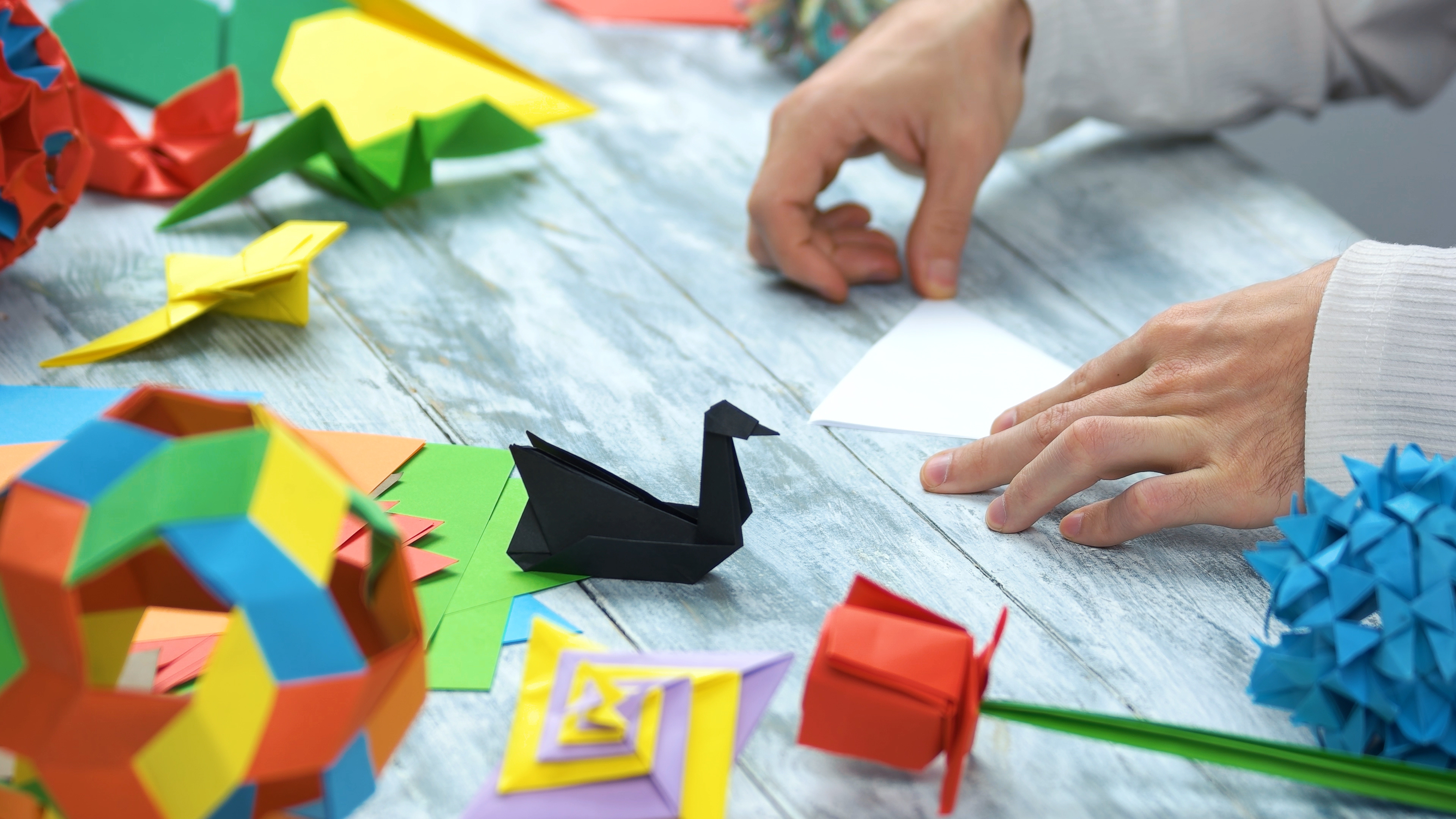 Hands folding paper with colorful origami figures on a table.