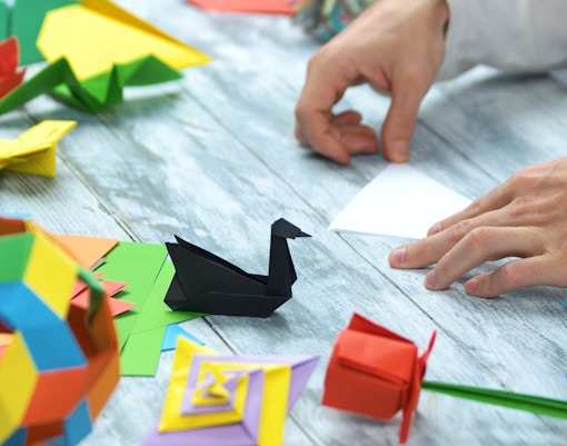 Hands folding paper with colorful origami figures on a table.