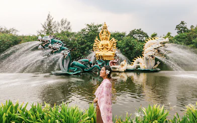Woman in traditional attire at Erawan Museum with dragon sculptures and golden deity statue.