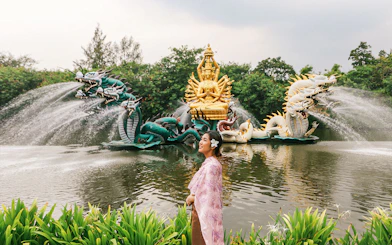 Woman in traditional attire at Erawan Museum with dragon sculptures and golden deity statue.