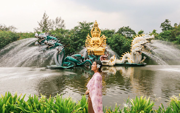 Woman in traditional attire at Erawan Museum with dragon sculptures and golden deity statue.