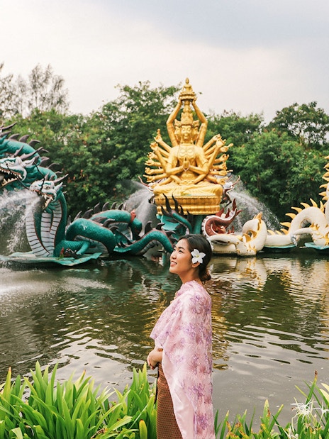 Woman in traditional attire at Erawan Museum with dragon sculptures and golden deity statue.