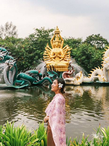Woman in traditional attire at Erawan Museum with dragon sculptures and golden deity statue.