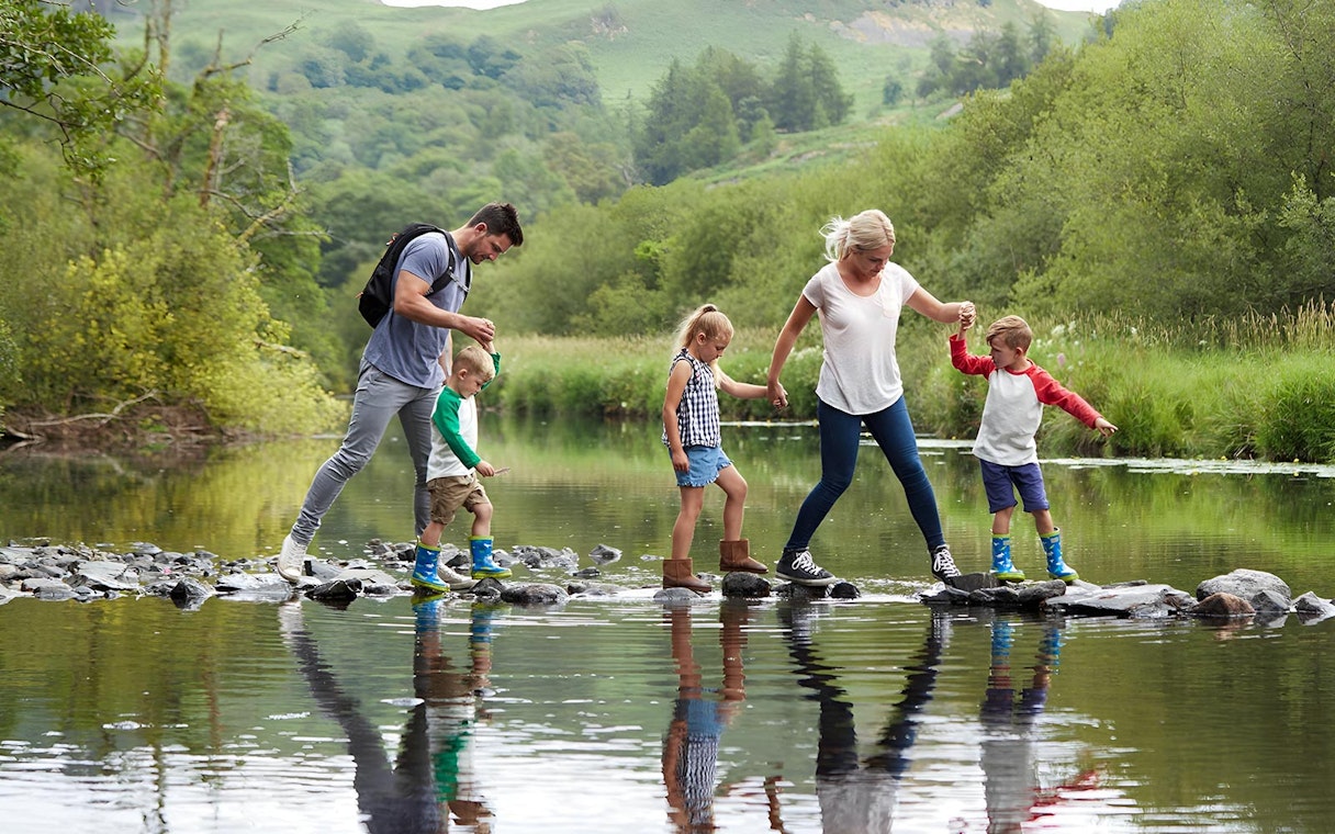 Family crossing a stream on stepping stones in the Lake District.