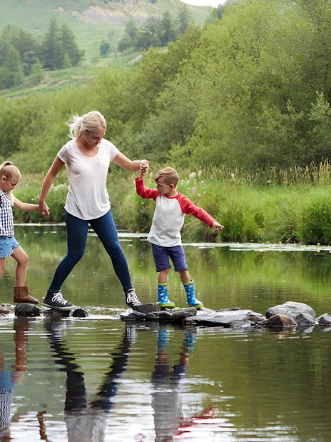 Family crossing a stream on stepping stones in the Lake District.