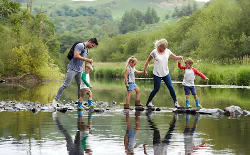 Family crossing a stream on stepping stones in the Lake District.