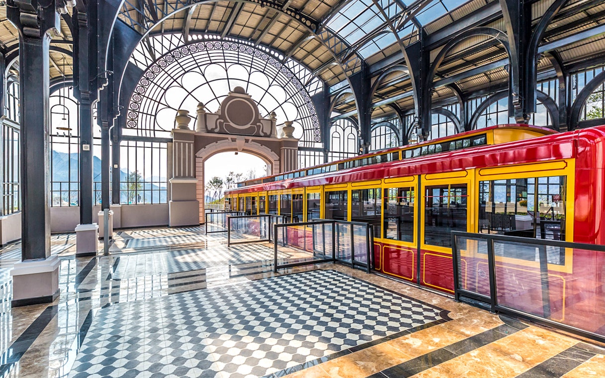 Red and yellow train inside Sun World Fansipan Legend station with arched glass roof.