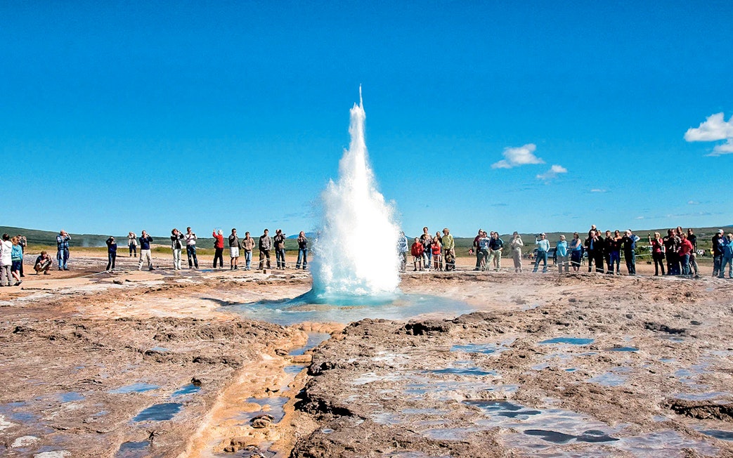 Geyser eruption at Strokkur, Iceland, with tourists observing during Golden Circle tour.