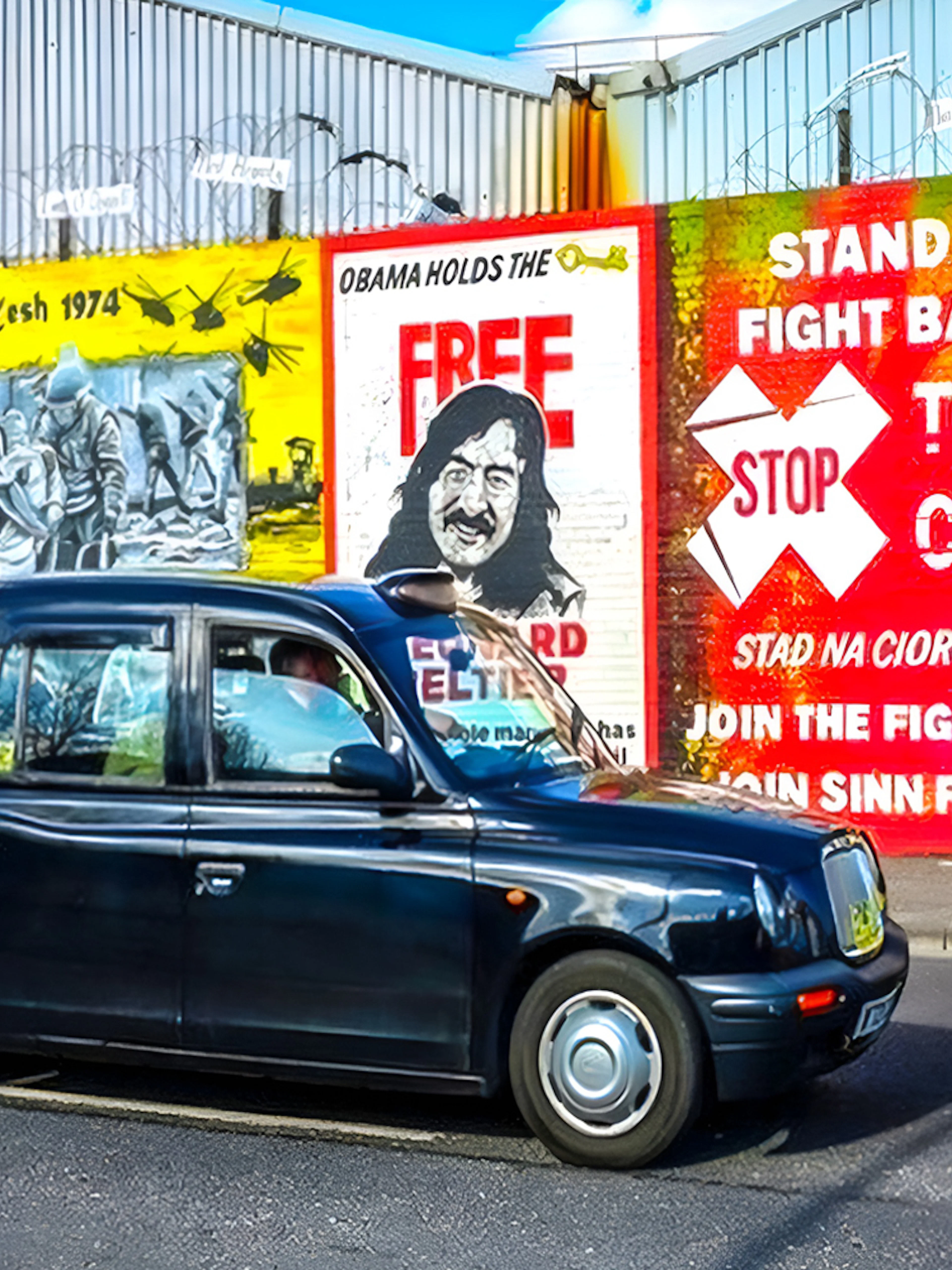 Black taxi in front of Belfast political murals during guided tour.