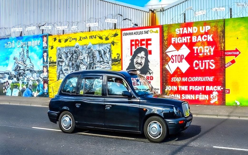 Black taxi in front of Belfast political murals during guided tour.