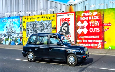 Black taxi in front of Belfast political murals during guided tour.