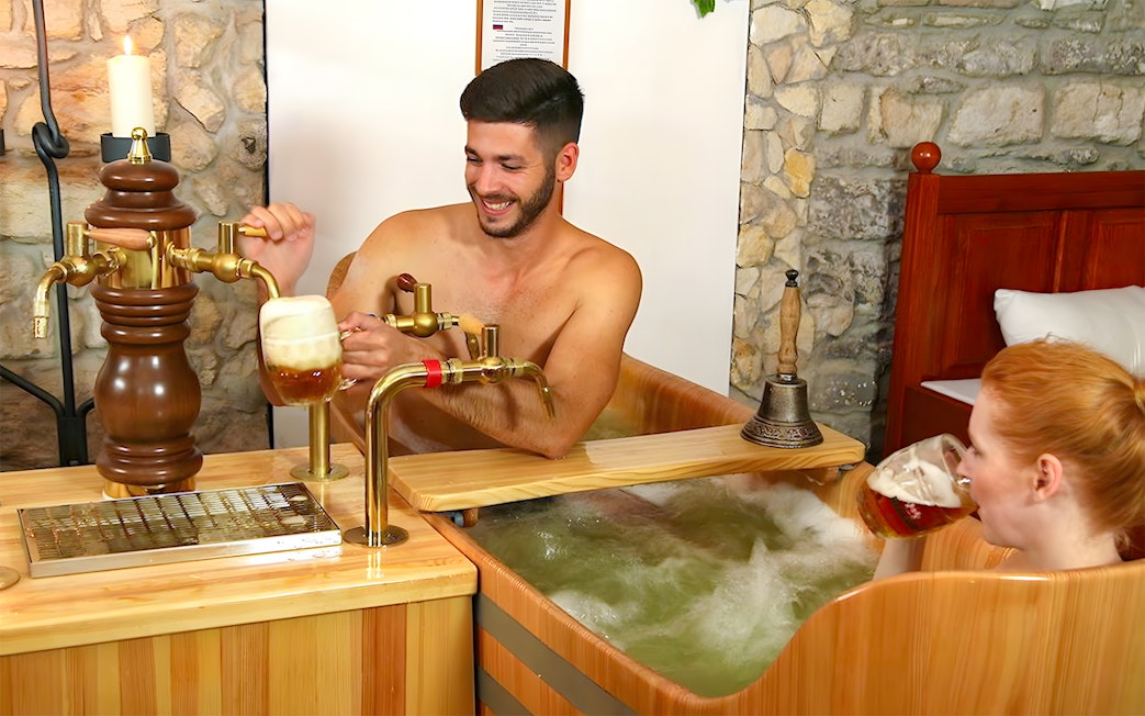 Couple enjoying a beer bath at Bernard Beer Spa with wooden tubs and beer taps.