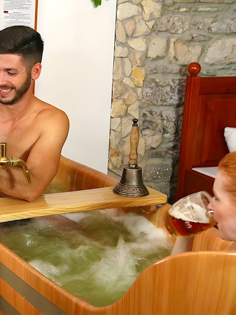 Couple enjoying a beer bath at Bernard Beer Spa with wooden tubs and beer taps.