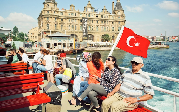 Cruise passengers on Bosphorus with Turkish flag and historic building in Istanbul.