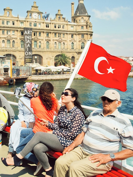Cruise passengers on Bosphorus with Turkish flag and historic building in Istanbul.