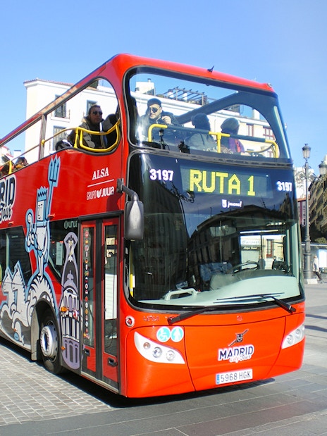 Red double-decker bus for Madrid Hop On Hop Off tour in city square.