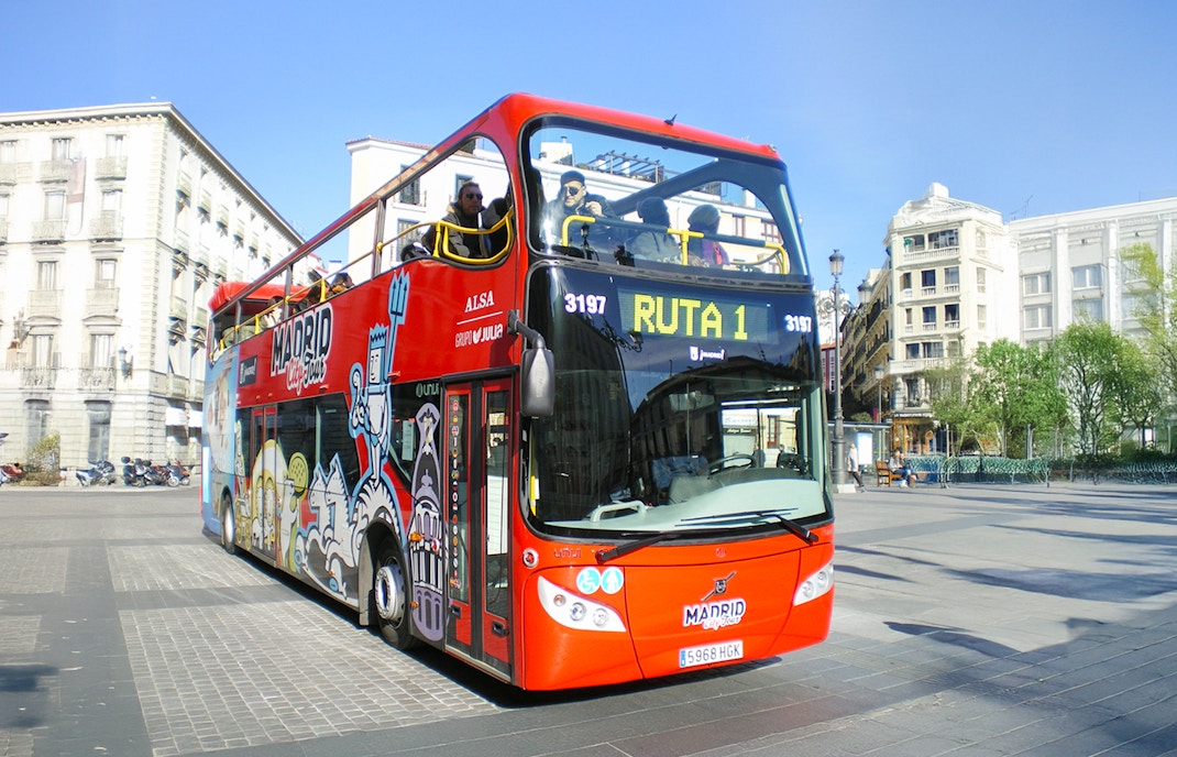 Red double-decker bus on Madrid Hop On Hop Off Bus Tour passing by historic city buildings.