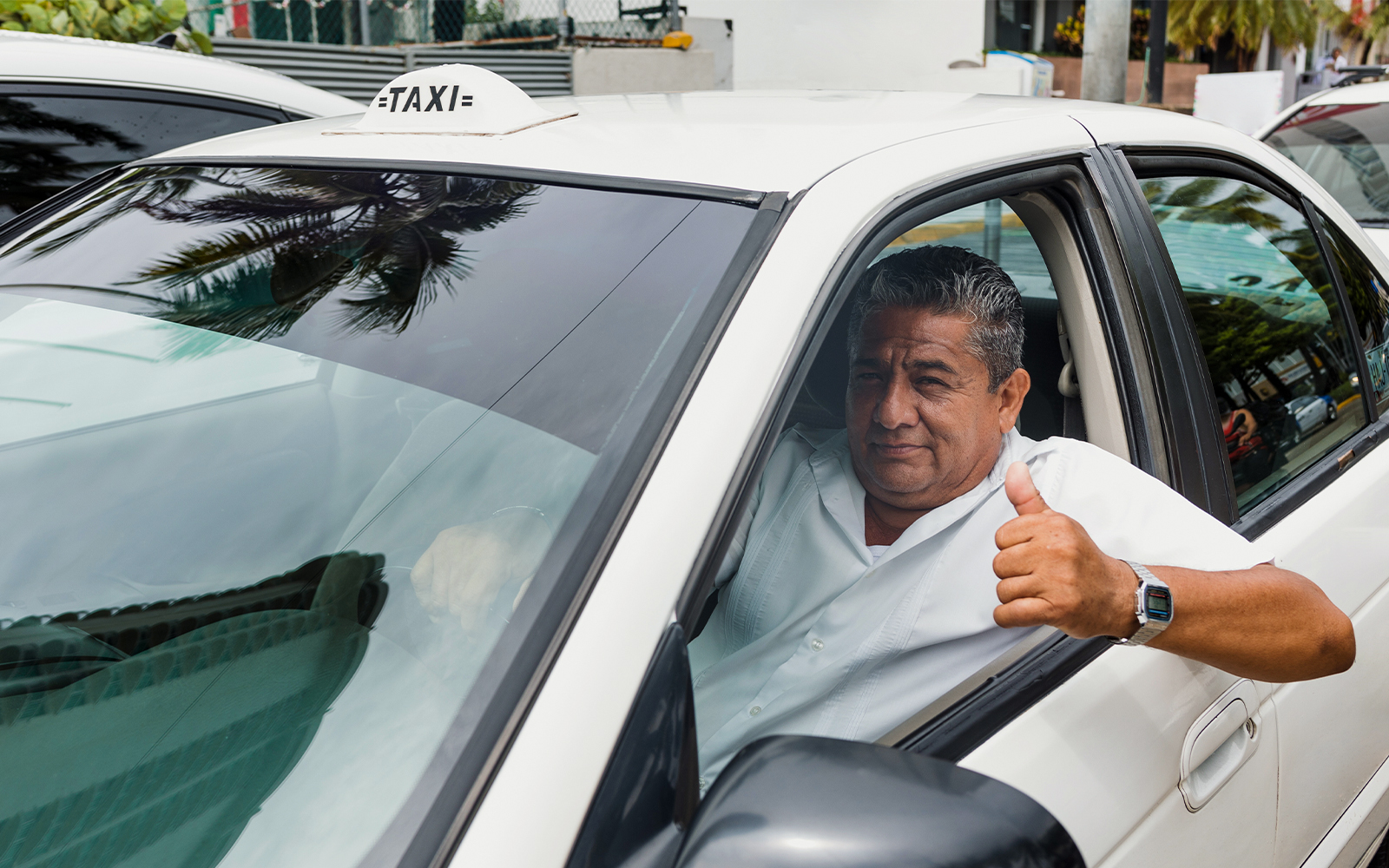 Senior taxi driver giving thumbs up in car on city street,
