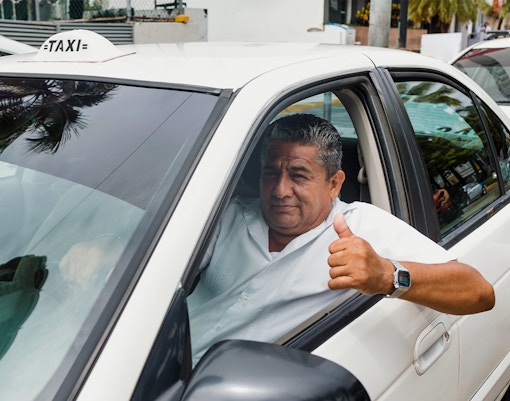 Senior taxi driver giving thumbs up in car on city street, Mexico.