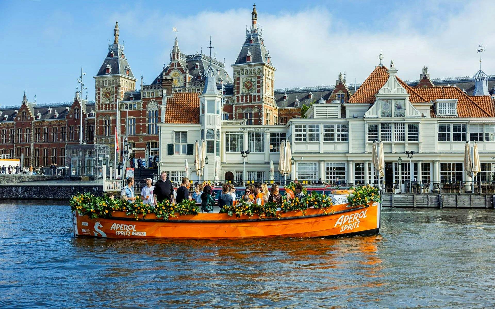 Guests enjoying Aperol Spritz Cruise on a canal in Amsterdam with historic buildings in the background.