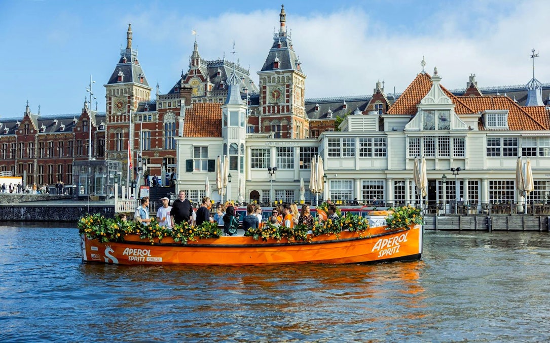 Guests enjoying Aperol Spritz Cruise on a canal in Amsterdam with historic buildings in the background.