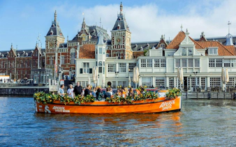 Guests enjoying Aperol Spritz Cruise on a canal in Amsterdam with historic buildings in the background.