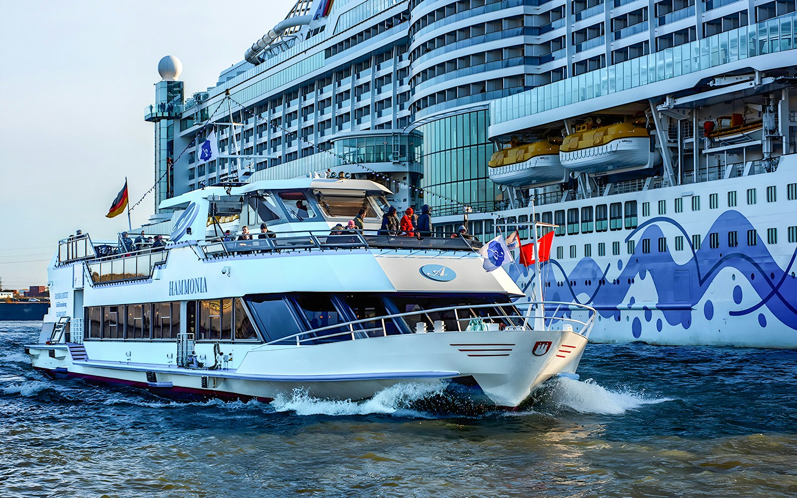 Cruise boat sailing in Hamburg harbor with a large ship in the background.