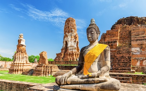 Statue of Buddha at Wat Mahathat, Ayutthaya, with ancient temple ruins in the background.