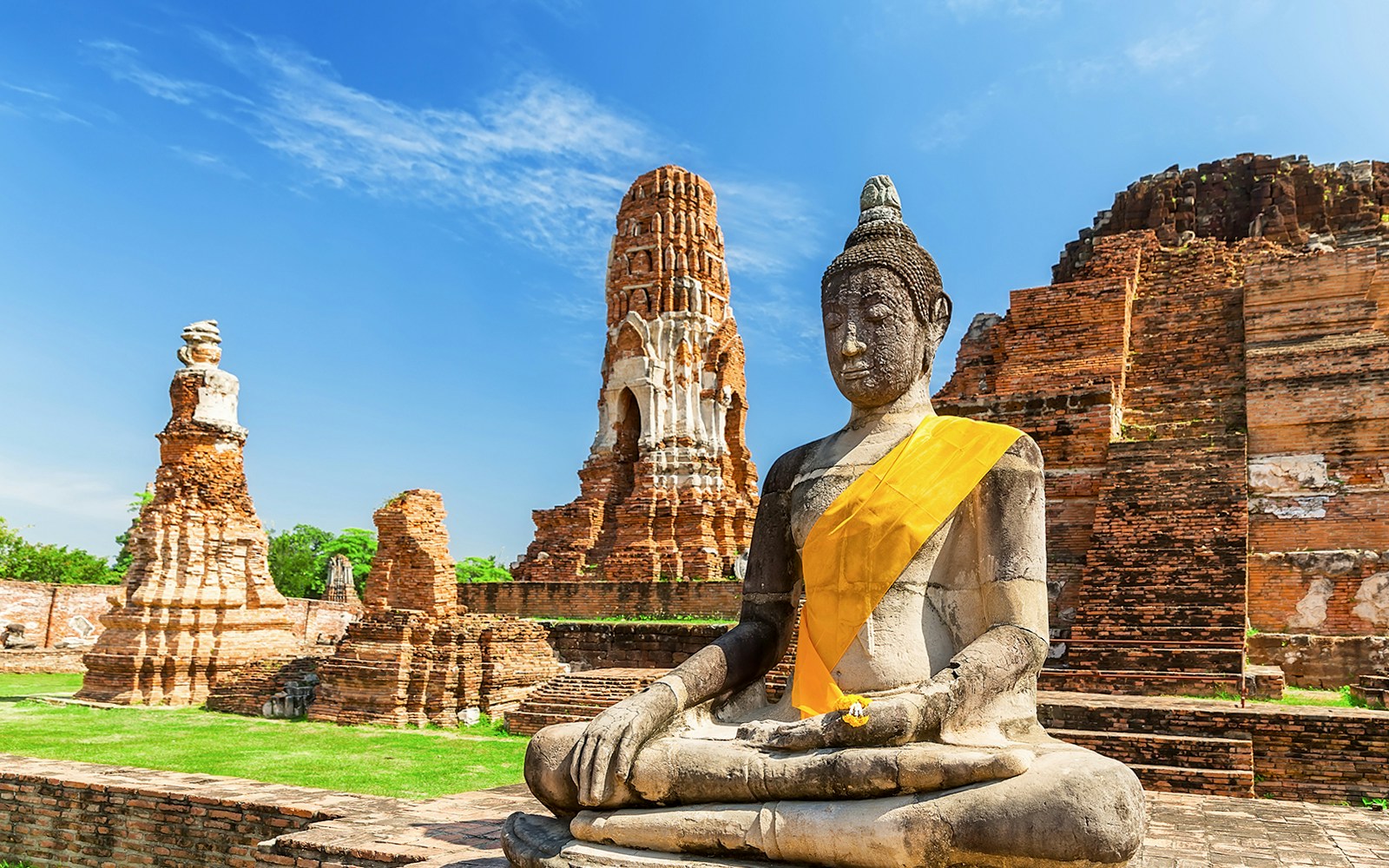 Statue of Buddha at Wat Mahathat, Ayutthaya, with ancient temple ruins in the background.