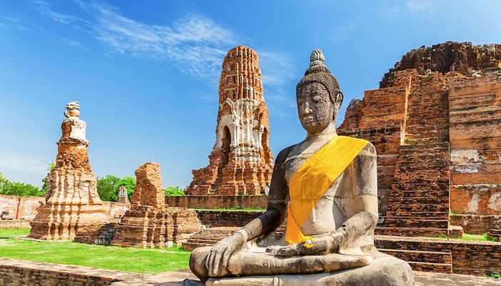 Statue of Buddha at Wat Mahathat, Ayutthaya, with ancient temple ruins in the background.