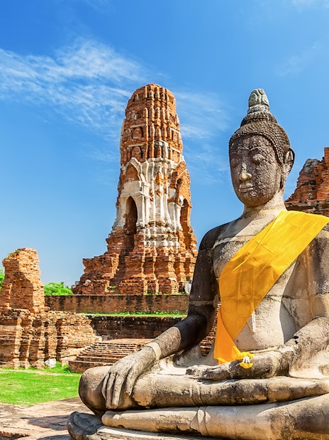 Statue of Buddha at Wat Mahathat, Ayutthaya, with ancient temple ruins in the background.