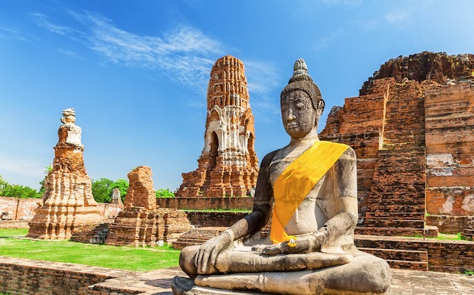 Statue of Buddha at Wat Mahathat, Ayutthaya, with ancient temple ruins in the background.