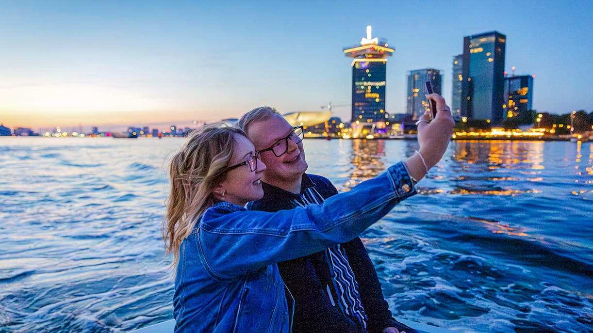 Guests taking a selfie on a winter evening cruise in Amsterdam with city skyline in the background.