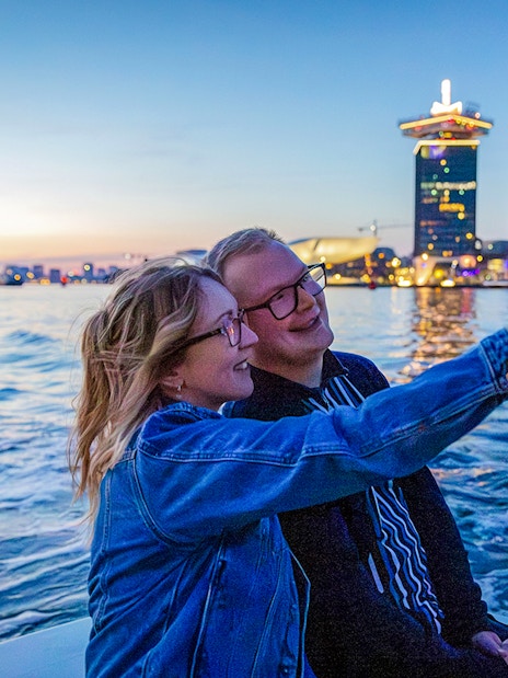 Guests taking a selfie on a winter evening cruise in Amsterdam with city skyline in the background.