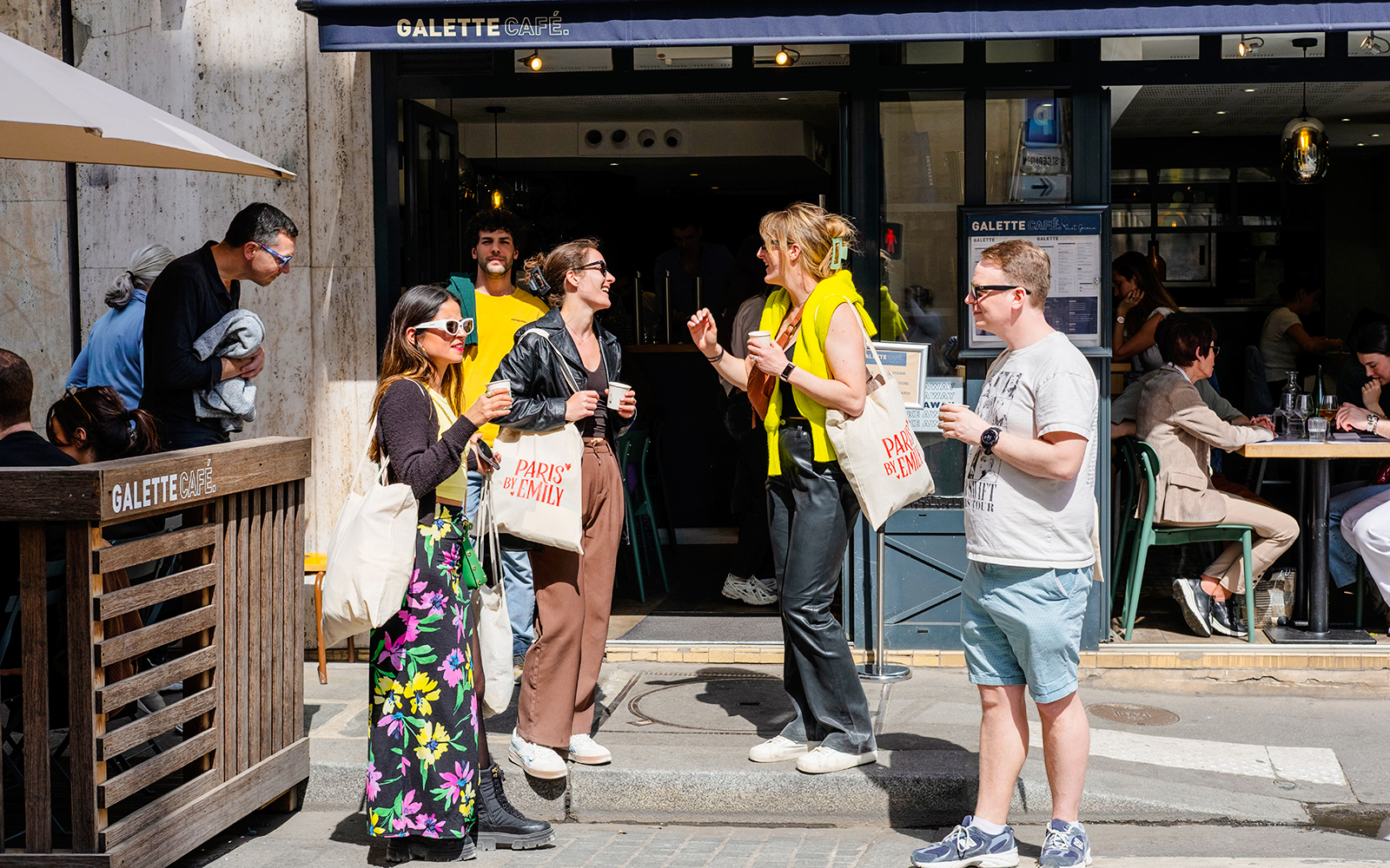 People outside Galette Café during Emily in Paris Food Tour, holding drinks and tote bags.