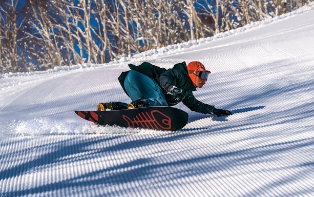 Snowboarder carving down a groomed slope at Niseko Resort, Japan.